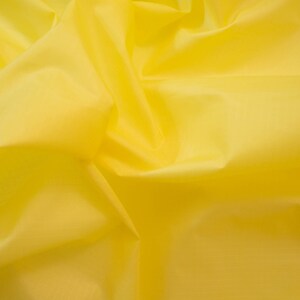 May include: A close-up of a bright yellow fabric with a smooth, silky texture. The fabric is folded and draped, creating soft, flowing lines.