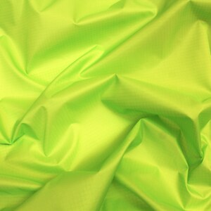 May include: A bright green fabric with a smooth, silky texture. The fabric is folded and draped, creating soft folds and wrinkles.