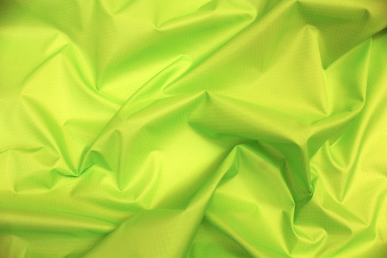May include: A bright green fabric with a smooth, silky texture. The fabric is folded and draped, creating soft folds and wrinkles.