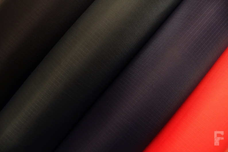 May include: Close-up of four fabric rolls in different colors: black, dark blue, light blue, and red. The fabric has a subtle texture.