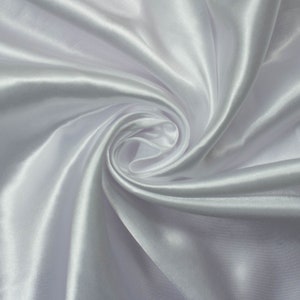 Puede incluir: Tela de satén blanco con una textura suave y sedosa. La tela está drapeada y doblada, creando curvas suaves y fluidas.