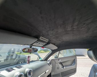 Può includere: Vista interna di un'auto, che mostra il rivestimento del tetto e il cruscotto grigio scuro, effetto pelle scamosciata. L'immagine include lo specchietto retrovisore, la visiera parasole e le bocchette dell'aria. La portiera è aperta, rivelando l'esterno.