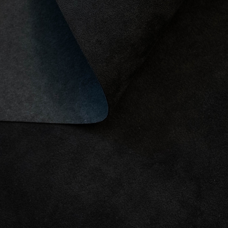 May include: Close-up of a black fabric with a soft, velvety texture. The fabric is folded in half, creating a smooth, curved line.