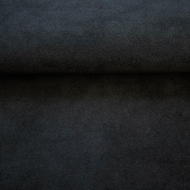 May include: Close-up of a dark gray fabric with a soft, fuzzy texture. The fabric is folded in half, showing the inside and outside of the material.