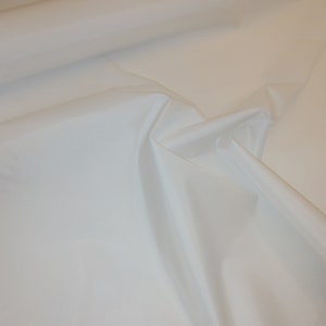 Puede incluir: Tela blanca con una textura suave y sedosa. La tela está doblada y drapeada, mostrando su calidad suave y fluida.