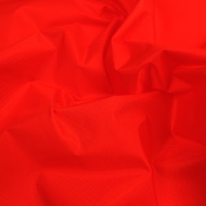 May include: A bright red fabric with a smooth, slightly textured surface. The fabric is wrinkled and folded, showing its drape and flexibility.
