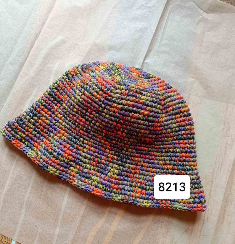 Puede incluir: Un gorro de cubo de crochet multicolor con una etiqueta que dice "8213".