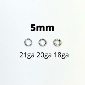 May include: Three silver-colored jump rings, each 5mm in diameter, are displayed against a white background. The text "5mm" is above the rings, and "21ga 20ga 18ga" is below. These rings are likely used for jewelry making or crafts.