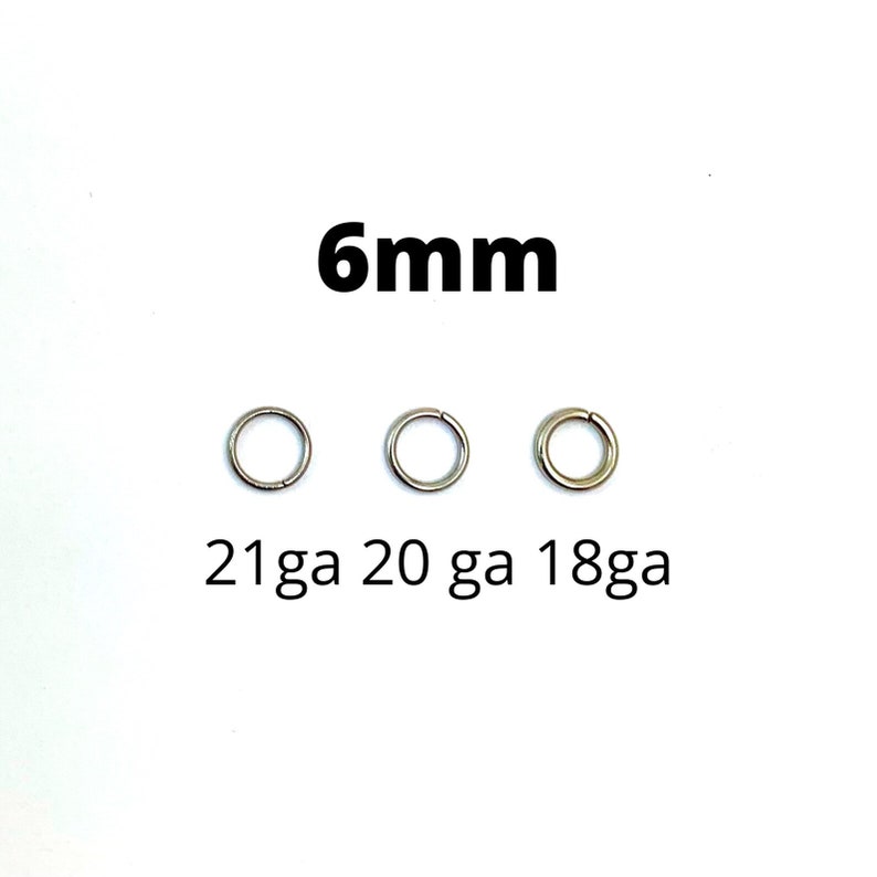 May include: Three silver-colored, circular body jewelry rings. The text "6mm" is above the rings, and below them are the text "21ga 20 ga 18ga". The rings are displayed on a white background.