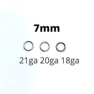 May include: Three silver-colored, circular rings with varying gauges (21ga, 20ga, 18ga) are displayed. The text "7mm" is above the rings, indicating their size. The rings are set against a plain white background.