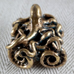 May include: A bronze-colored octopus figurine with blue accents. The octopus has detailed tentacles and a textured surface. The figurine is a decorative item, possibly for a nautical-themed collection.
