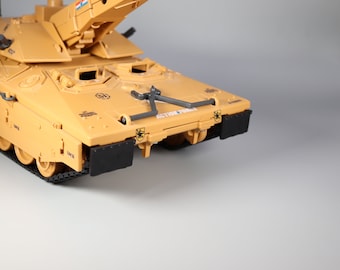 Peut inclure: Maquette de char d'assaut de couleur beige avec des chenilles et des détails noirs. La maquette présente une tourelle surélevée et le texte "ACTION FORCE" est visible. Des panneaux noirs sont présents à l'avant.