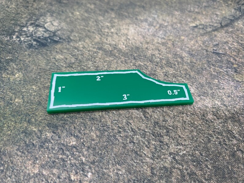 Peut inclure: Un gabarit en plastique vert avec des lignes blanches et des mesures en pouces. Le gabarit a la forme d'un rectangle avec un bord incurv&eacute;. Les mesures sont de 1", 2", 3" et 0,5".