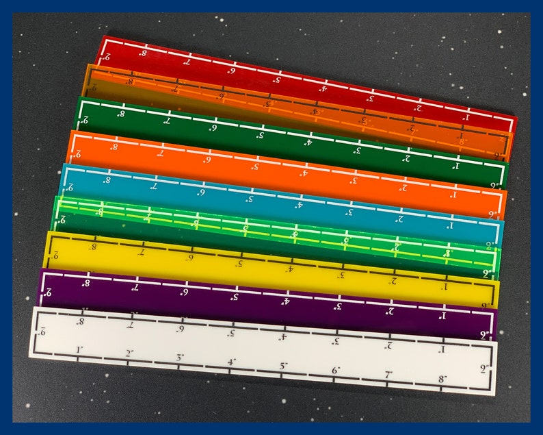 May include: A collection of colorful, transparent rulers in various colors, including red, orange, green, blue, yellow, purple, and white. Each ruler is 9 inches long and has inch and fractional inch markings.