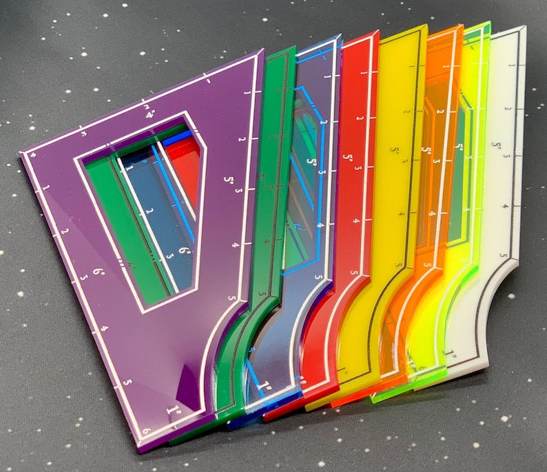 K&ouml;nnte beinhalten: Ein Satz von sieben bunten Plastiklinealen mit verschiedenen Markierungen und Formen. Die Lineale sind f&auml;cherf&ouml;rmig angeordnet, wobei das violette Lineal oben und das gelbe Lineal unten liegt. Die Lineale sind alle transparent und haben wei&szlig;e Markierungen.