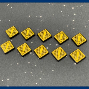 May include: Ten yellow square game tokens with black borders and a yellow exclamation point symbol. The tokens are arranged on a dark gray surface with white speckles.