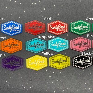 May include: A set of 12 hexagonal shaped logo stickers in various colours, including blue, red, green, orange, turquoise, pink, purple, yellow, and black and white. Each sticker features the text "Surly Good Designs" in white lettering.