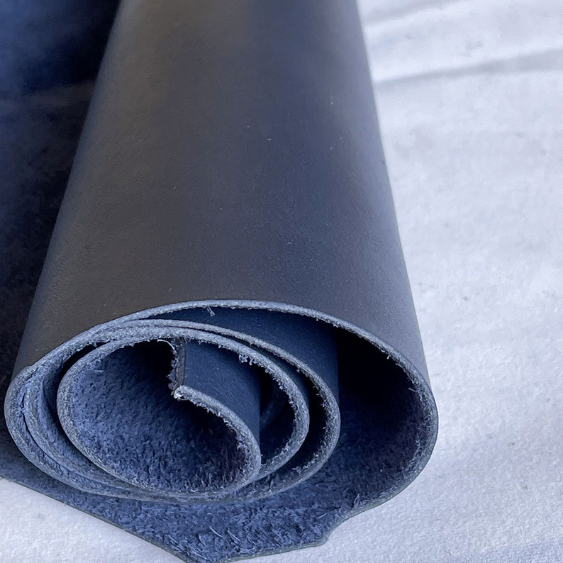 Pode incluir: Um peda&ccedil;o enrolado de couro azul marinho. O couro tem um acabamento liso e fosco no exterior e um verso texturizado, semelhante a camur&ccedil;a. As bordas do couro s&atilde;o vis&iacute;veis, mostrando as camadas do material enrolado.