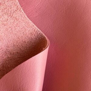 May include: Close-up of a pink leather material with a textured surface. The leather is folded over, revealing the soft, suede-like underside.