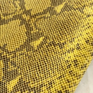 Peut inclure: Tissu en peau de serpent jaune avec un motif brun foncé. Le tissu a une surface texturée et écailleuse.