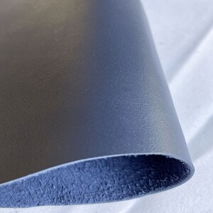 Pode incluir: Um close-up de um peda&ccedil;o de couro azul marinho. O couro tem uma superf&iacute;cie texturizada e um gr&atilde;o vis&iacute;vel. A parte inferior do couro &eacute; um tom mais escuro de azul. O couro &eacute; provavelmente usado para artesanato ou estofamento.