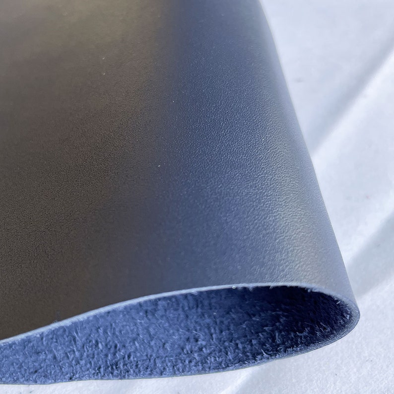 Pode incluir: Um close-up de um peda&ccedil;o de couro azul marinho. O couro tem uma superf&iacute;cie texturizada e um gr&atilde;o vis&iacute;vel. A parte inferior do couro &eacute; um tom mais escuro de azul. O couro &eacute; provavelmente usado para artesanato ou estofamento.