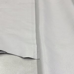 May include: A close-up of a white leather fabric. The fabric has a smooth, slightly textured surface.