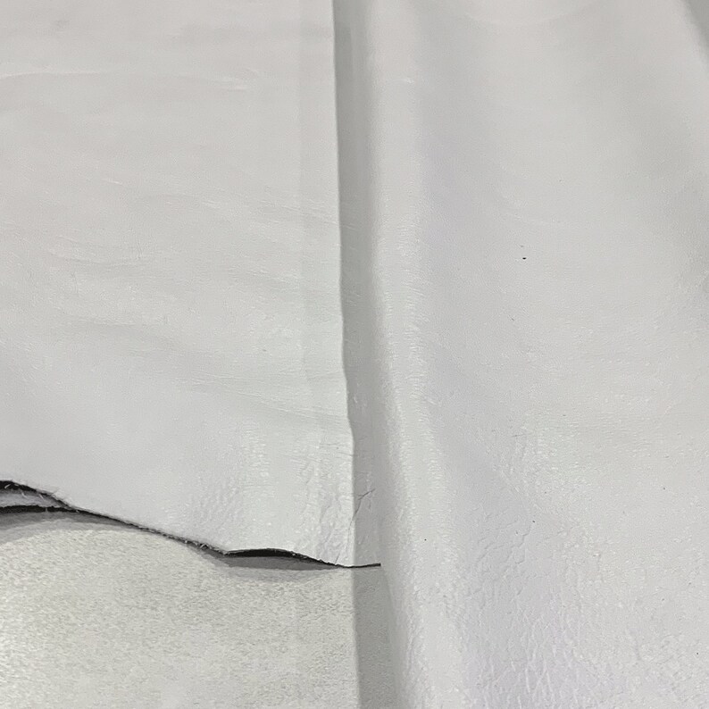 May include: A close-up of a white leather fabric. The fabric has a smooth, slightly textured surface.