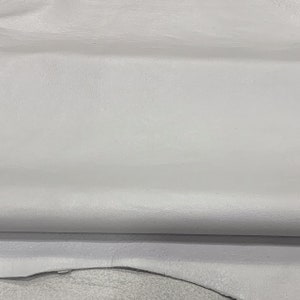 May include: A close-up of a piece of white leather with a textured surface. The leather is folded in half, showing the underside.