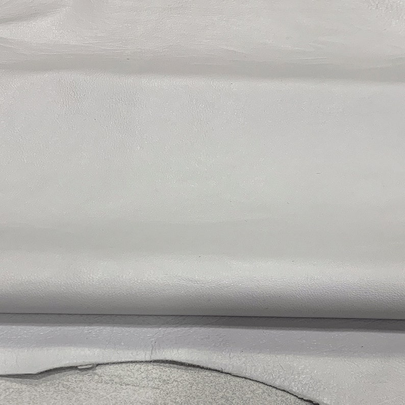 May include: A close-up of a piece of white leather with a textured surface. The leather is folded in half, showing the underside.