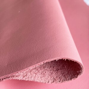 May include: Close-up of a pink leather sheet with a textured surface. The leather is folded over, revealing the soft, fuzzy underside.