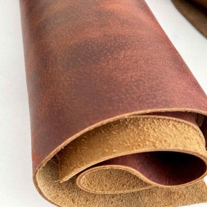 May include: Close-up of a rolled piece of brown leather with a reddish-brown hue. The leather has a natural, textured surface.