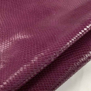 May include: A close-up of a piece of purple snakeskin leather. The leather has a textured surface and a glossy finish.