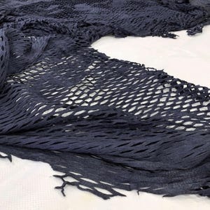 May include: Dark navy blue fabric with a unique openwork design. The fabric has a net-like pattern with diamond-shaped openings. The edges of the fabric are fringed, adding texture. This textile is suitable for various craft and design projects.