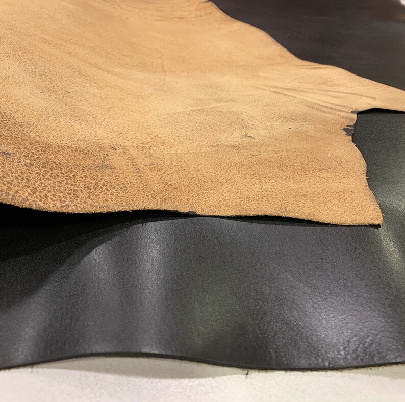 K&ouml;nnte beinhalten: Zwei Lederst&uuml;cke, eines braun und eines schwarz, liegen &uuml;bereinander gefaltet. Das braune Leder hat eine strukturierte Oberfl&auml;che.