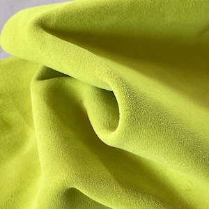 Könnte beinhalten: Nahaufnahme eines gefalteten, hellgrünen Stoffes. Der Stoff hat eine weiche, samtige Textur und einen leichten Glanz. Die Falten erzeugen Schatten und Lichtreflexe, die die Textur und Farbe des Materials hervorheben.