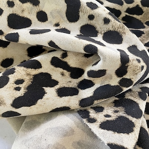 Könnte beinhalten: Nahaufnahme eines beigefarbenen Stoffes mit einem schwarzen Leopardenmuster. Der Stoff ist gefaltet und texturiert.