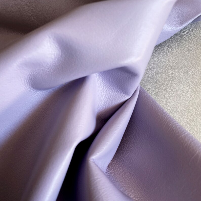 May include: A close-up of a soft, light purple leather fabric. The fabric is folded and draped, showing its texture and color.