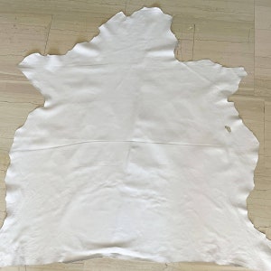 May include: A white leather hide with a slightly irregular shape. The leather is smooth and appears to be soft.