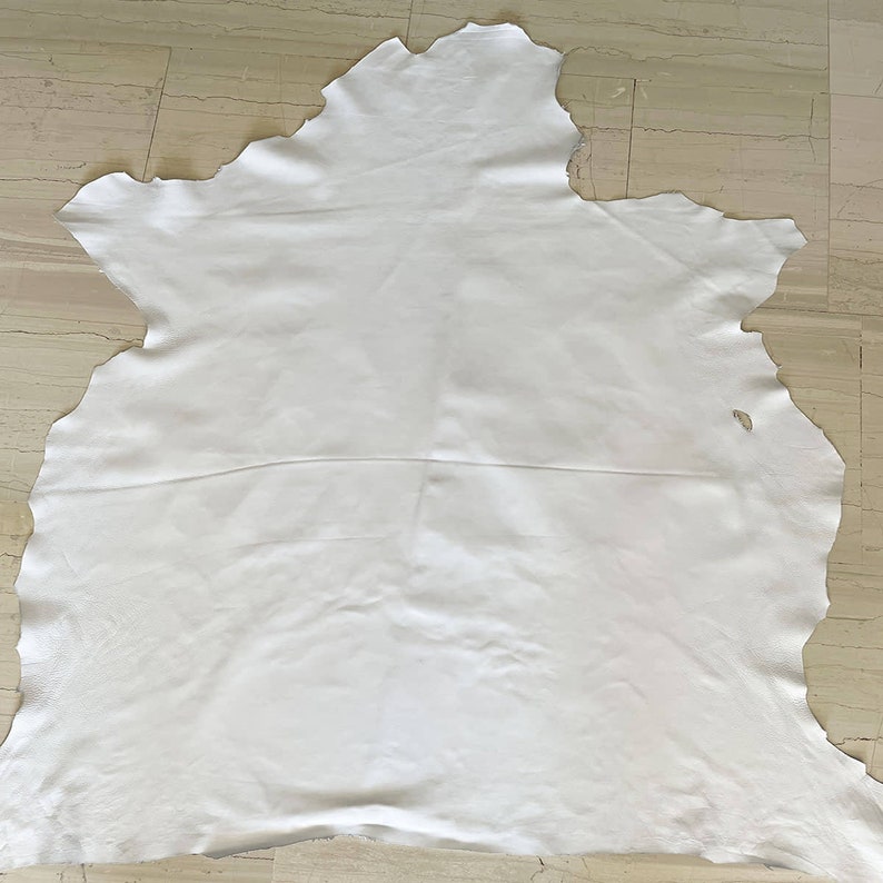 May include: A white leather hide with a slightly irregular shape. The leather is smooth and appears to be soft.
