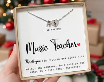 May include: A silver necklace with the letter "A" and a musical note charm, presented in a gift box. The box features the text "Music Teacher" and a message of appreciation, making it a thoughtful gift.