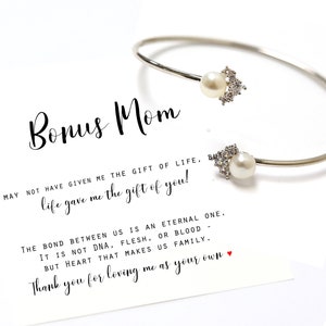 May include: A silver bangle bracelet with two pearl and crystal accents. The bracelet is accompanied by a card with the text "Bonus Mom You may not have given me the gift of life, but life gave me the gift of you! The bond between us is an eternal one. It is not DNA, flesh, or blood but heart that makes us family. Thank you for loving me as your own."