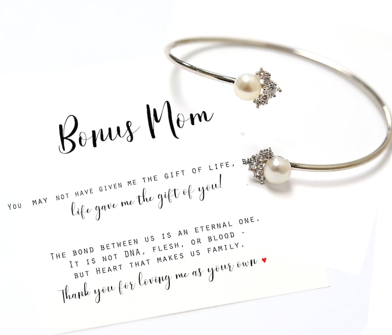 May include: A silver bangle bracelet with two pearl and crystal accents. The bracelet is accompanied by a card with the text "Bonus Mom You may not have given me the gift of life, but life gave me the gift of you! The bond between us is an eternal one. It is not DNA, flesh, or blood but heart that makes us family. Thank you for loving me as your own."