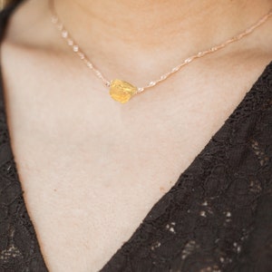 May include: A delicate gold chain necklace with a raw, yellow gemstone pendant.