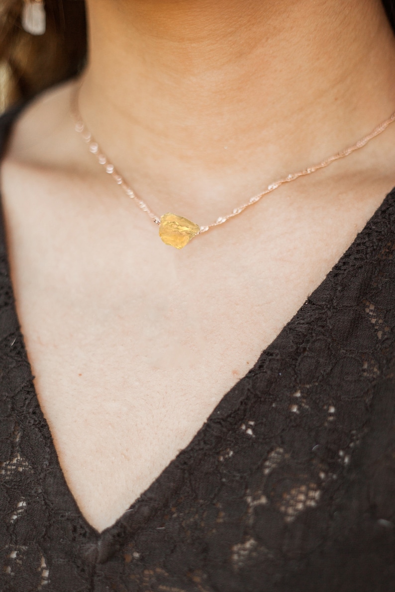 May include: A delicate gold chain necklace with a raw, yellow gemstone pendant.