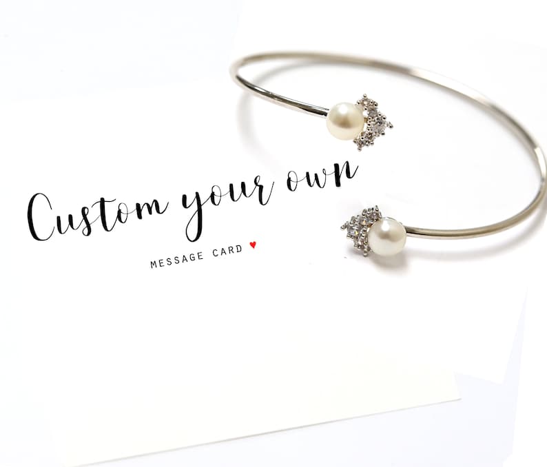 May include: Silver bangle bracelet with two pearl and crystal accents. The bracelet is on a white card with the text "Custom your own" and "Message Card".