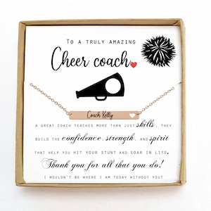 May include: A rose gold necklace with a rectangular pendant engraved with "Coach Kelly" and a heart. The necklace is presented in a gift box with text that reads "To a truly amazing Cheer coach". A black megaphone and a pom-pom are also featured.