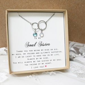 May include: A silver necklace with two interlocking circles, each with a small gemstone pendant. The necklace is presented in a gift box with the text "To my Soul Sister" and a heartfelt message.