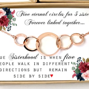 May include: A rose gold necklace with five interconnected circles, presented in a box with a floral design and the text "Five eternal circles for 5 sisters Forever linked together... TRUE Sisterhood IS WHEN five PEOPLE WALK IN DIFFERENT DIRECTIONS BUT REMAIN SIDE BY SIDE".
