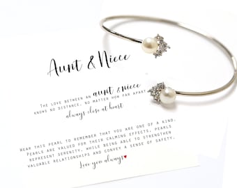 May include: Silver bracelet with two pearl charms and a message card that reads "Aunt & Niece The love between an aunt & niece knows no distance, no matter how far apart always close at heart Wear this pearl to remember that you are one of a kind. Pearls are valued for their calming effects, pearls represent serenity, while being able to strengthen valuable relationships and convey a sense of safety. Love you always"